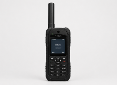 Front-facing rugged black satellite phone with long antenna, numeric keypad, and small display screen showing ‘Iridium Registered,’ placed on a plain light gray background in a clean studio product shot.